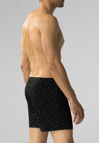 Czarne bokserki z drobnym zielonym wzorem liści, wykonane z gładkiej tkaniny, z elastycznym paskiem w pasie i dopasowanym kształtem.