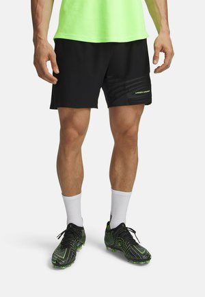 Zwarte atletiekshorts met een gestructureerd ontwerp en een geel logo, gecombineerd met zwarte en neon groene voetbalschoenen en witte sportsokken.