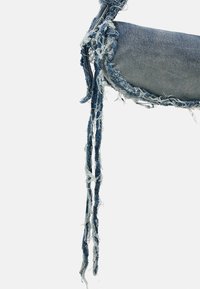 Denim torba z zaobljenim oblikom, s frayed robovi in dolgimi, obrabljenimi modrimi trakovi. Svetlo in temno moder odtenek z vidno teksturo.