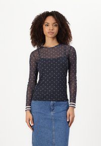 Marineblauwe longsleeve top met een doorzichtige overlay, voorzien van een geometrisch patroon en gestreepte manchetten. Gecombineerd met een denim rok.