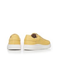 Sneaker in pelle gialla con finitura testurizzata, suola in gomma bianca, punta rotonda e design delle stringhe minimalista. La vista laterale mostra il collare imbottito.