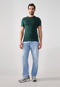 Grønn kortermet skjorte kombinert med lyseblå denimjeans og sølvfargede joggesko. Enkelt design, tettsittende skjorte og avslappet passform på jeansene.