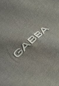 Material gri cu aspect texturat, având marca „GABBA” gravată în relief, de culoare gri deschis. Design curat, concentrat pe detaliul siglei.