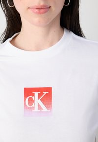 Witte katoenen t-shirt met een centrale vierkante graphic in een verloop van rood naar roze, met de letters "cK" in het wit. Ronde halslijn en korte mouwen.