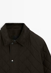 Svart quiltad jacka med en kordflodderskrage, tryckknappsstängning och diamantmönstrad textur.