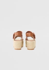 Sandales à plateforme en cuir marron avec un talon en jute tressé et une bride de cheville, présentant une boucle latérale et une finition texturée.