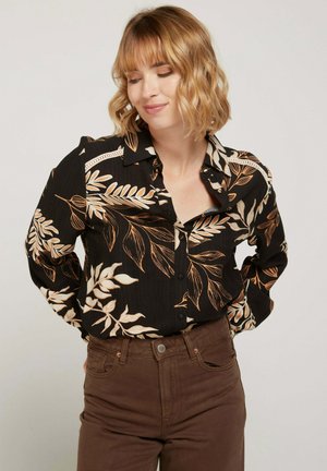 Chemise noire à manches longues avec des motifs floraux beiges, en tissu texturé et à col, assortie à un pantalon taille haute marron.