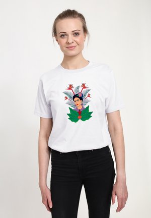 Bílý bavlněný tričko s barevným květinovým a portrétním motivem, se zelenými listy a červeným srdcem. Model nosí černé kalhoty.