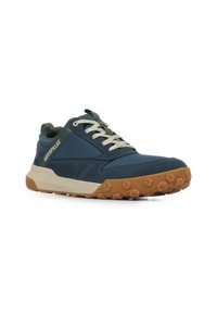 Blauwe stoffen sneaker met een gestructureerde afwerking, een beige rubberen buitenzool en groene accenten op de tong en het logo. Voorzien van veters en stikseldetails.