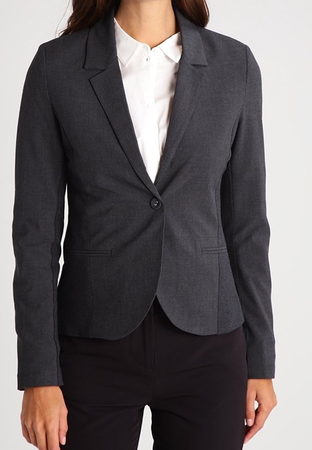 Femme portant un blazer gris foncé ajusté sur une chemise blanche boutonnée et un pantalon noir, montrée du cou aux hanches.