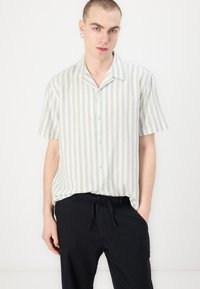 Īsām piedurknēm, pogām aizdara krekls gaismas zaļā un baltā svītrā, ar nometnes apkakli un mīkstu audumu. Valkāts ar tumšām biksēm.