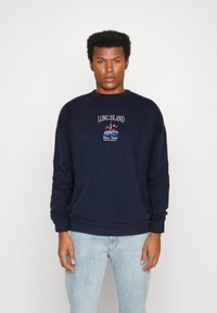 Sudadera azul marino de mezcla de algodón, con cuello redondo, mangas largas y diseño bordado de "LONG ISLAND" y un faro en la parte frontal.