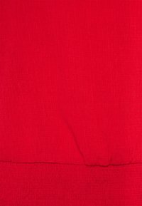 Rød tekstureret stof med et krøllet mønster. Materialet er let og har en samlet søm i bunden.