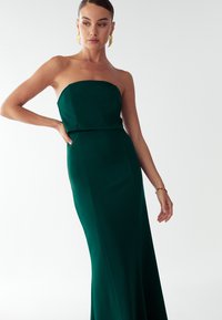 Sukienka bez ramiączek sięgająca do podłogi, wykonana z bujnej zielonej tkaniny, z dopasowanym gorsetem i gładką sylwetką o subtelnej fakturze.