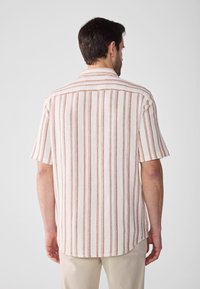 Camicetta a maniche corte in tessuto crema con righe verticali rosse, dotata di colletto e orlo dritto sul retro. Materiale testurizzato.