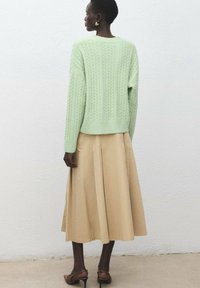 Mintovo zelený sveter s káblovým vzorom a voľným strihom, kombinovaný s béžovou plisovanou sukňou a hnedými lodičkami. Jemná textúra a mäkká tkanina.