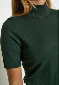 Tmavě zelený krátký rukáv turtleneck svetr vyrobený z žebrované pleteniny, s přiléhavým střihem a žebrovanými detaily na rukávech.