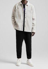 Jasnoszara, wełniana kurtka na guziki z dwoma przednimi kieszeniami, zestawiona z czarnymi dresami i białymi trampkami dla casualowego wyglądu.