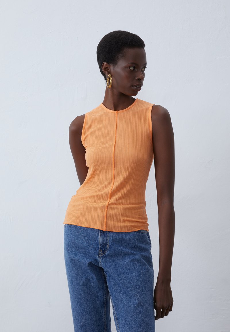 Orange ribbed sleeveless top featuring a round neckline and central seam, paired with blue high-waisted jeans. Smooth texture and fitted design.