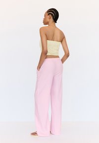 Haut smocké sans bretelles jaune clair associé à un pantalon large rose pâle, décontracté, avec poches latérales.