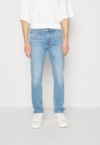 Jeans de mezclilla azul claro, corte recto, diseño de cinco bolsillos, con un lavado sutil, combinados con una camiseta blanca y zapatillas claras.