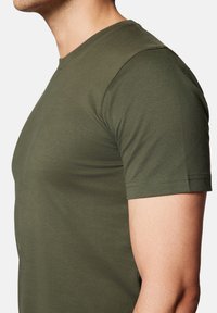 Oliwkowa koszulka z krótkim rękawem wykonana z miękkiej bawełny, z okrągłym dekoltem i dopasowanym krojem, który podkreśla sylwetkę.