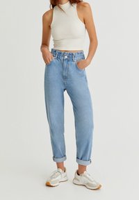 Jeans de mezclilla azul claro con cintura alta, dobladillos enrollados y bolsillos laterales. Combinados con un top de halter blanco de canalé y zapatillas grises.
