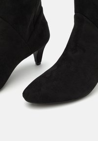 Bottines à talons en daim noir avec un bout pointu et un petit talon effilé. Texture lisse et lignes épurées dans un design minimaliste.