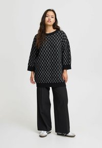 Pull noir oversize avec un motif en diamant en blanc et bleu clair, associé à un pantalon large noir et des baskets blanches.