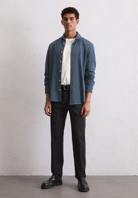 Blauwe overhemden met een witte t-shirt eronder, zwarte broek, zwarte schoenen. Het overhemd heeft een kraag en lange mouwen.