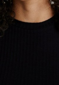 Top nero a costine con collo alto e tessuto testurizzato, che mette in risalto morbide curve al colletto e una linea morbida attorno al collo.