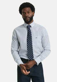 Gestreiftes Hemd aus weißer und blauer Baumwolle, mit einem Button-Down-Kragen, Brusttasche und kombiniert mit einer marineblauen gestreiften Krawatte.
