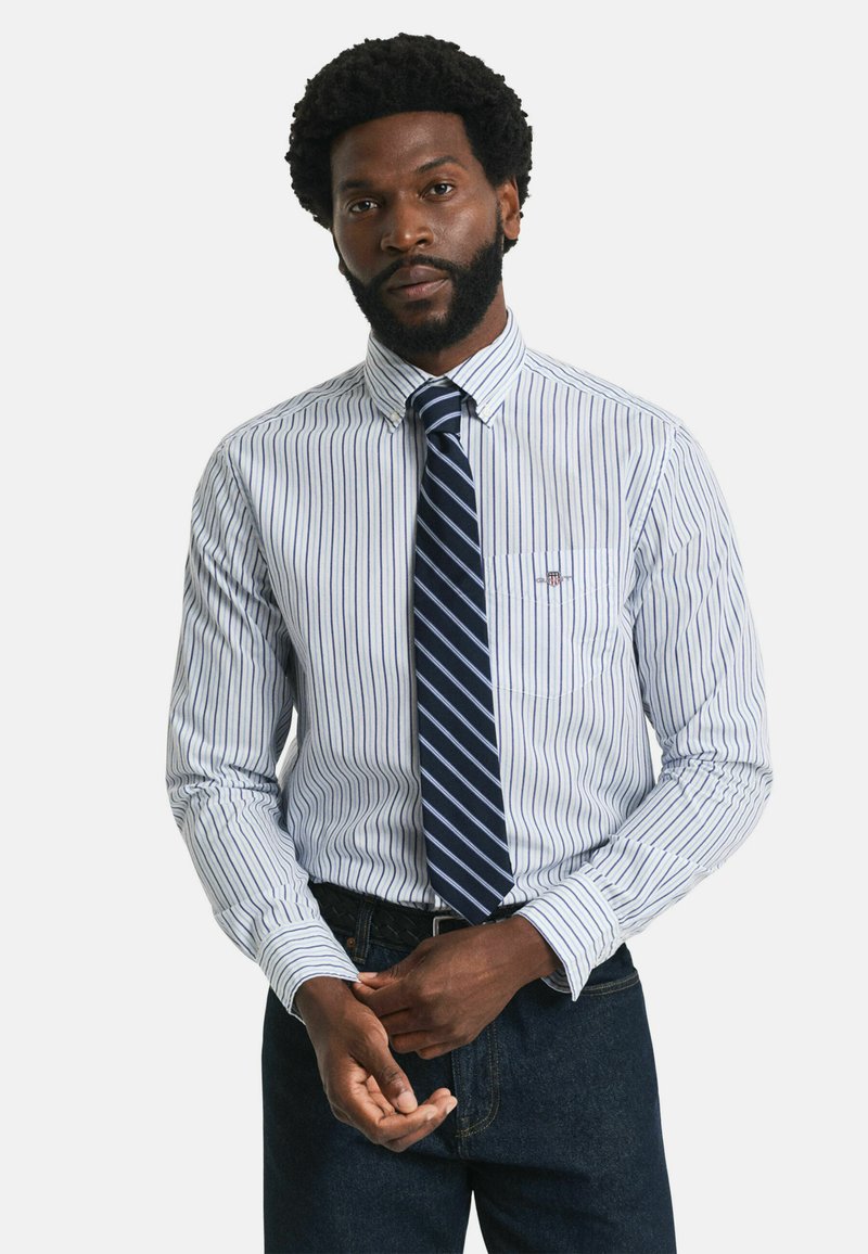 Chemise à rayures en coton blanche et bleue, avec un col boutonné, une poche poitrine et accompagnée d'une cravate rayée bleu marine.