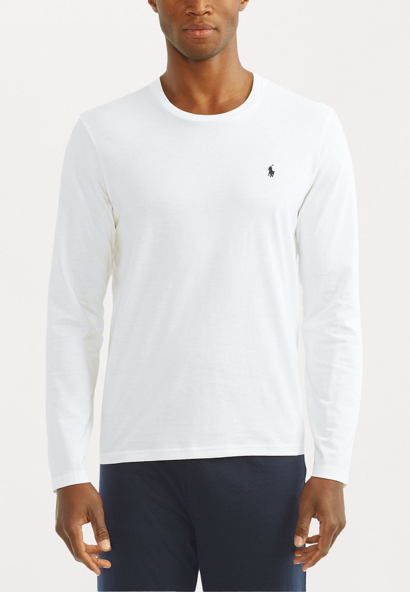 Long-sleeve white T-shirt, cotton material, crew neck, fitted style, features a small black logo on the left chest. Pairing with dark pants.