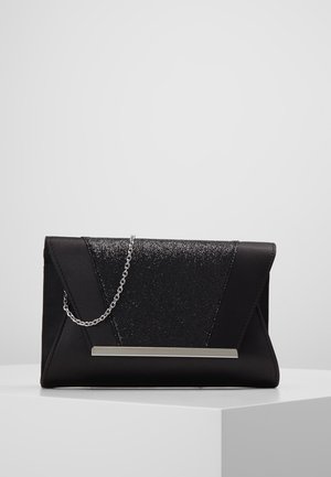 Pochette noire forme enveloppe avec panneau pailleté, bandoulière chaîne argentée et détail barre métallique horizontale sur un piédestal blanc.