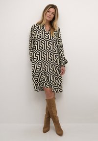 Vestido de estampado geométrico en crema y negro. Con mangas largas y escote en V. Combinado con botas de caña alta en marrón claro.