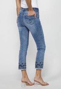 Jean en denim bleu clair au design court ; ourlet effiloché orné de broderies et de décorations ; quatre poches et fermeture éclair.