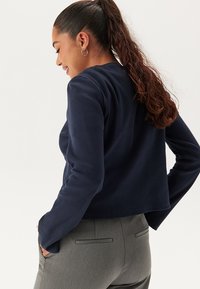 Navyblaues, geripptes Langarmoberteil mit lässiger Passform, rundem Ausschnitt und strukturiertem Stoff, kombiniert mit grauen, maßgeschneiderten Hosen.