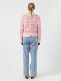 Maglione lavorato a maglia in pattern a zigzag rosa e crema con colletto e orlo a coste; indossato con jeans a vita alta azzurri e scarpe nere.