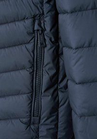 Marineblaue Steppjacke mit einer Reißverschlusstasche mit schwarzen Zipperzähnen und kontrastierenden Nähten. Gequiltete Textur mit isolierender Polsterung.