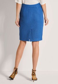 Blaue, gerippte Bleistiftrock mit Schlitz hinten und tailliertem Bund, kombiniert mit braunen Riemchen-Heels. Glatte Textur und maßgeschneiderter Schnitt.