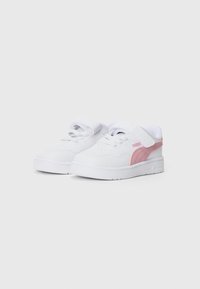 Zapatillas blancas para niños pequeños con una franja del logo de Puma en rosa, cordones y tira de Velcro sobre fondo gris claro.