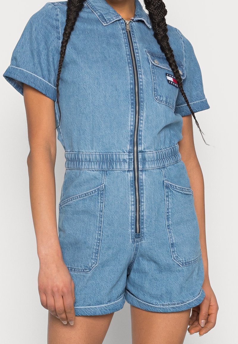 Jeansbyxdress med korta ärmar, framdragkedja, elastisk midja och två framfickor; ljusblå färg med subtil textur.