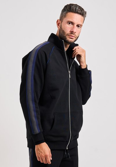 Felpa nera con zip e collo alto, caratterizzata da strisce laterali blu e grigie. Ha tasche frontali e una texture morbida.