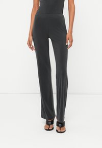 Pelēki, mīksti auduma bikses ar pieguļošu jostasvietu, izplestām kājām un gludu tekstūru. Valkā ar melniem, siksnu sandaļiem.