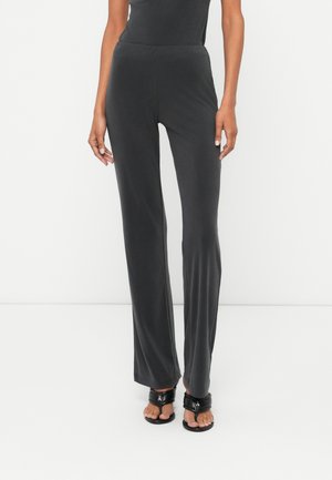 Graue, weiche Stoffhosen mit einer taillierten Taille, ausgestellten Beinen und glatter Textur. Tragen mit schwarzen, römischen Sandalen.