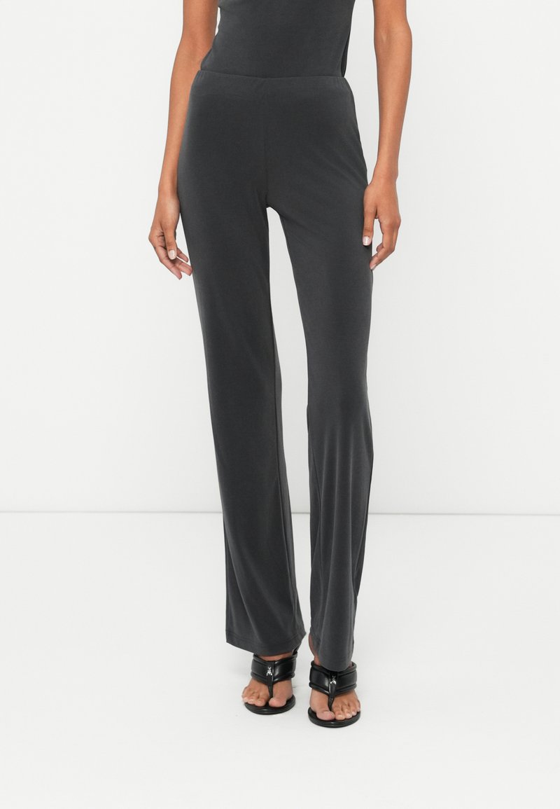 Pelēki, mīksti auduma bikses ar pieguļošu jostasvietu, izplestām kājām un gludu tekstūru. Valkā ar melniem, siksnu sandaļiem.