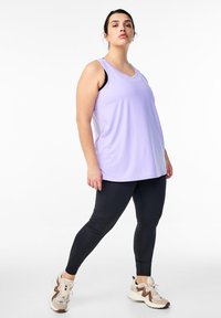 Helles lila ärmelloses Oberteil, kombiniert mit schwarzen Leggings und beigen Turnschuhen. Das Oberteil hat einen runden Ausschnitt; die Leggings haben eine glatte Textur.
