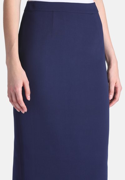 Femme portant une jupe crayon bleu marine ajustée, unie, avec une taille haute et un tissu lisse, montrée de la taille au milieu de la cuisse.