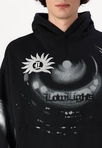 Schwarzer Hoodie mit abstrakten grauen Mustern, der ein Sonnenlogo mit dem Buchstaben "L" in der Mitte zeigt. Weicher Stoff mit lässigem Schnitt.